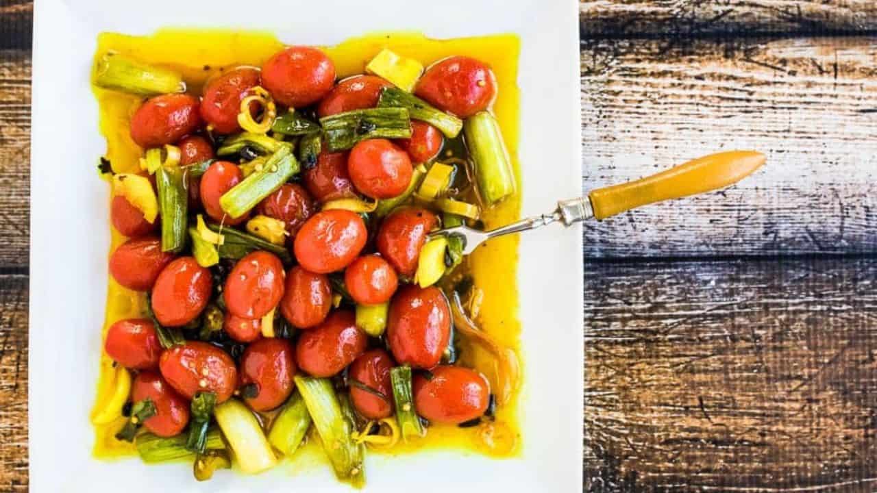 Quick Pickled Turmeric Tomatoes on a white plate with a hand lifting a spoonful.