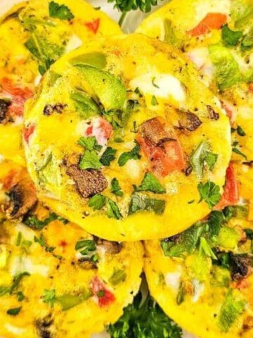 A white dish filled with colorful egg muffins topped with chopped vegetables and herbs, garnished with parsley.