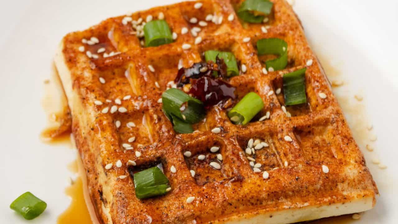 An overhead image of waffle tofu on a plate, garnished with scallions and soy sauce mixture.