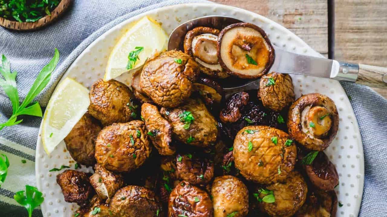 Air fryer shiitake and cremini mushrooms on a plate with lemon wedges.