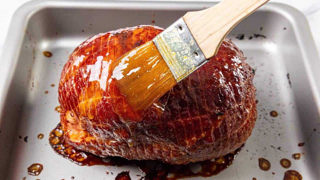 A metal roasting pan holds a baked ham covered with a glossy glaze.