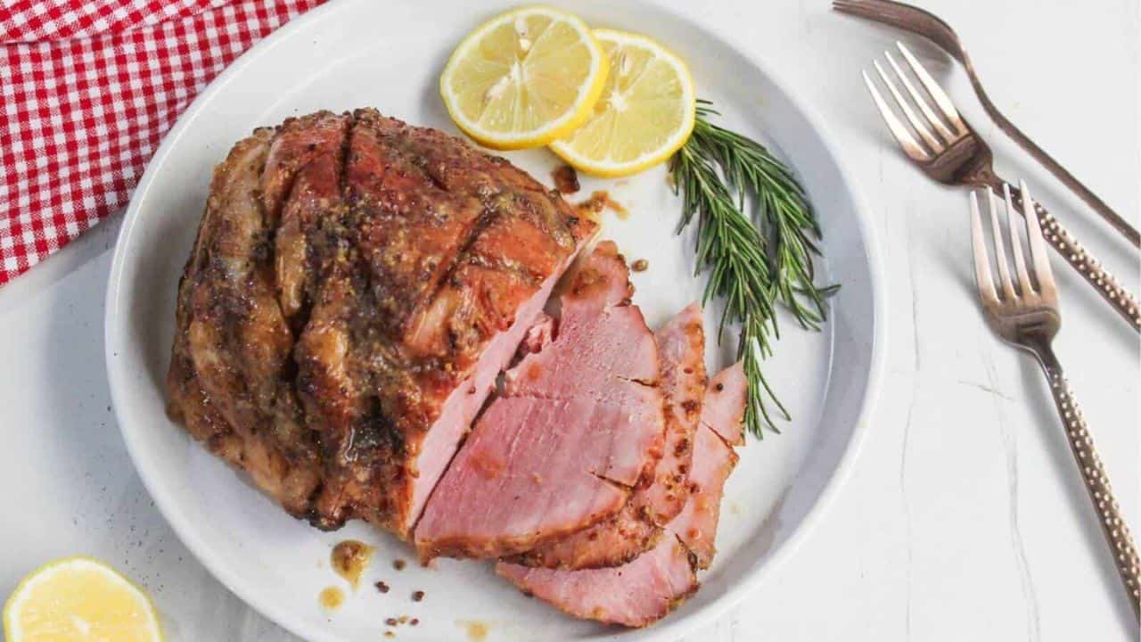 Sliced roasted ham garnished with sprigs of rosemary on a white plate.