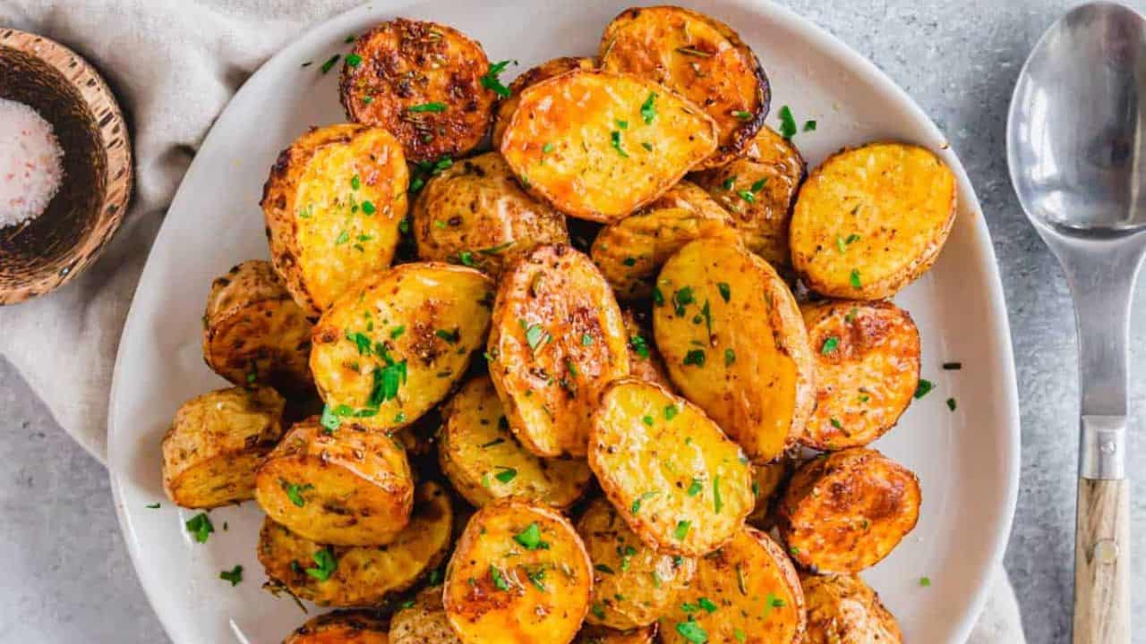 Golden roasted air fryer baby potatoes on a serving plate with a wooden and metal spoon.