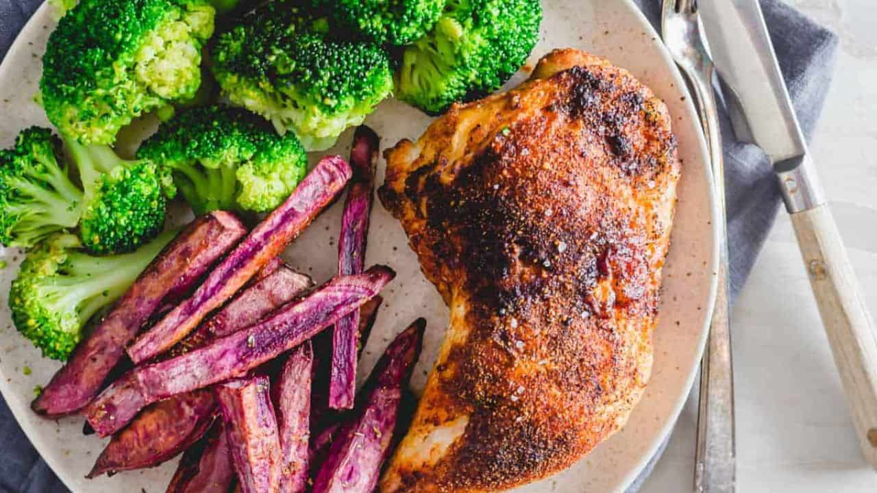 Air fryer chicken leg quarters on a plate with broccoli and purple sweet potato fries.