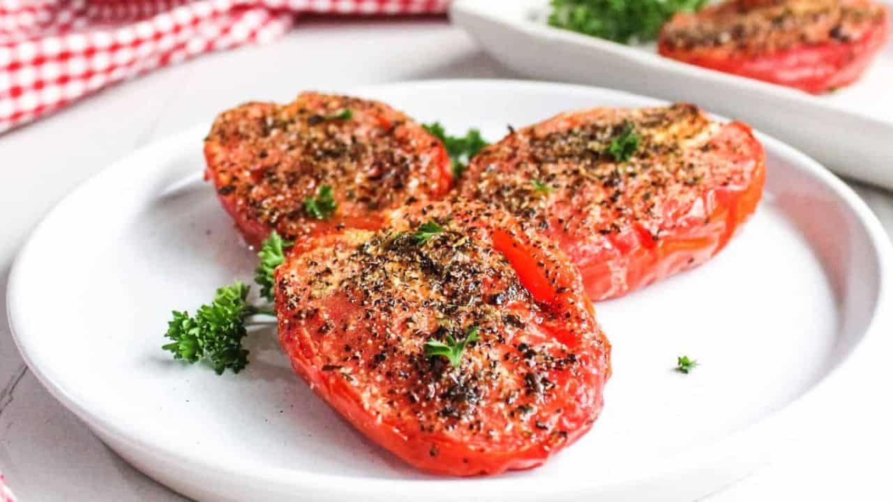 Roasted tomatoes seasoned with herbs and spices, served on a white plate garnished with parsley.