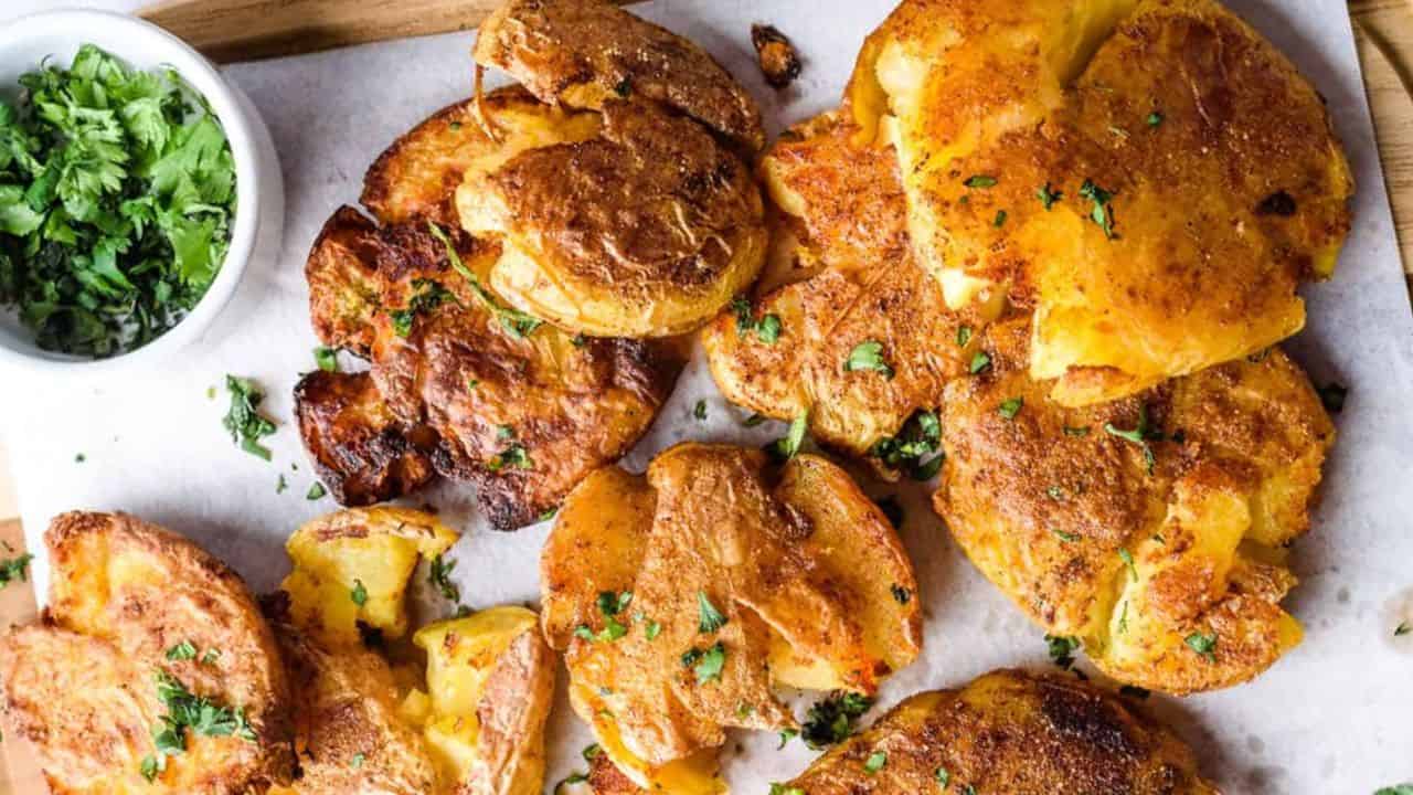 Smashed potatoes on a wooden board, crispy and golden, topped with fresh herbs.