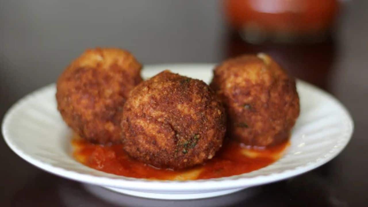 Plate of arancini with marinara and broccolini blurred in background.
