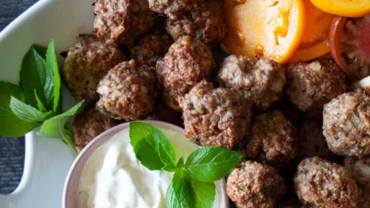 Baked turkey meatballs with tomato slices, pita bread, dipping sauce, and fresh mint.
