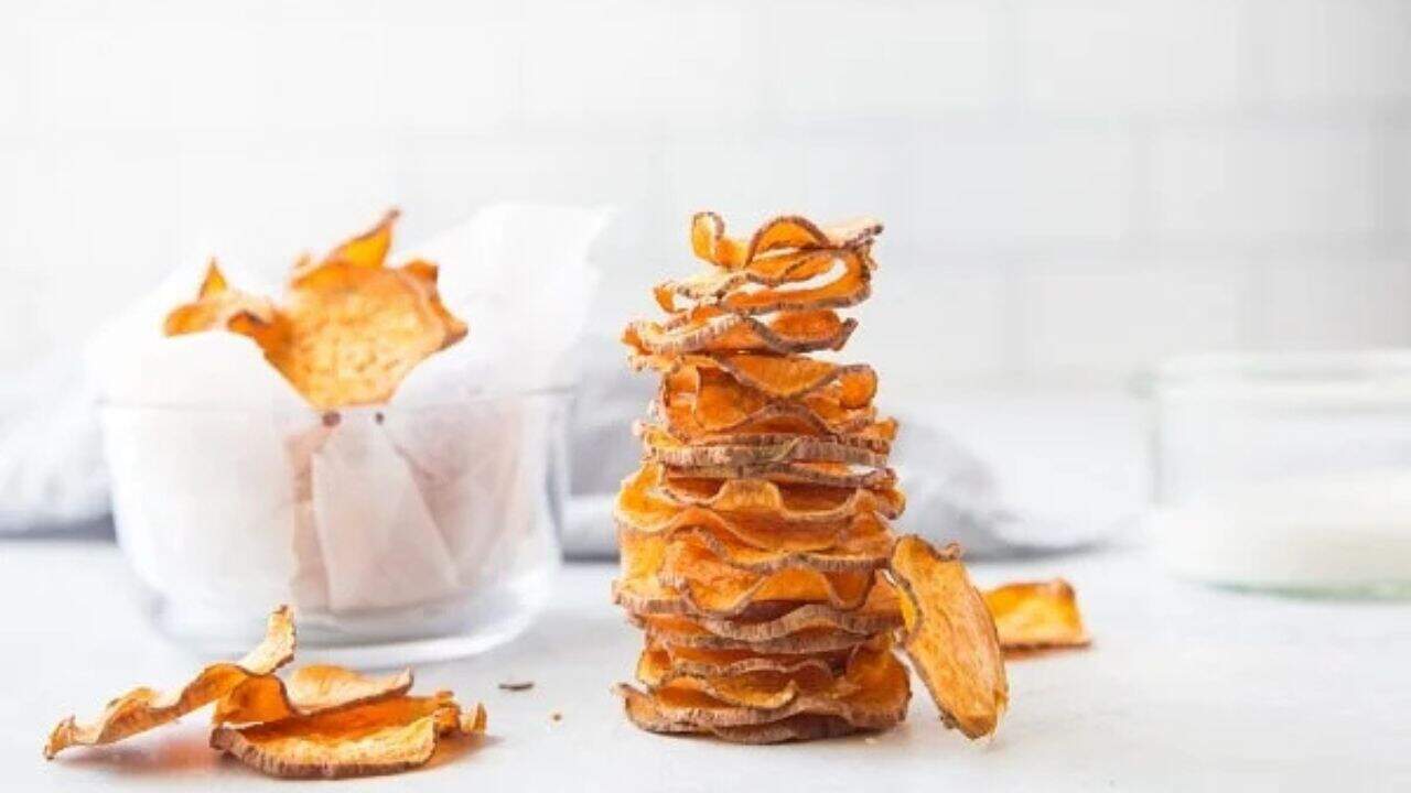 A stack of sweet potato chips next to a glass of milk.