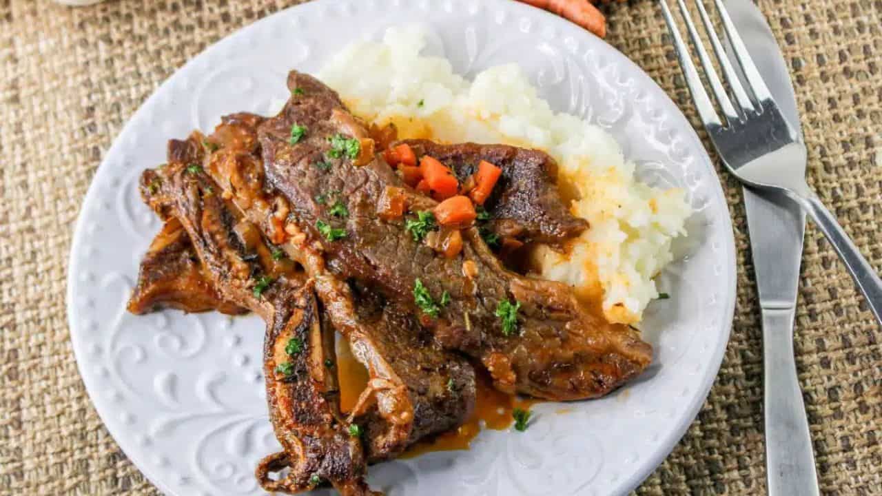 Beer braised short ribs on a plate on top of a bed of mashed potatoes.