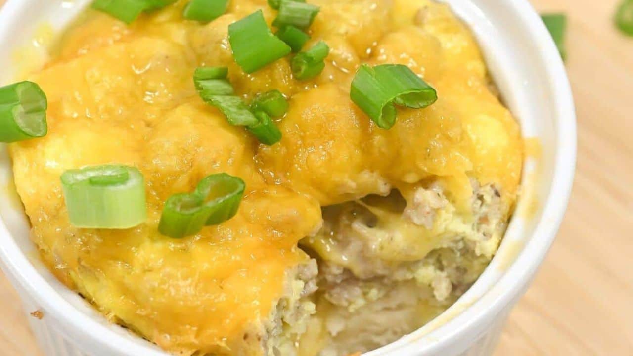 A white bowl filled with a cheesy, layered casserole topped with melted cheddar cheese and chopped green onions.