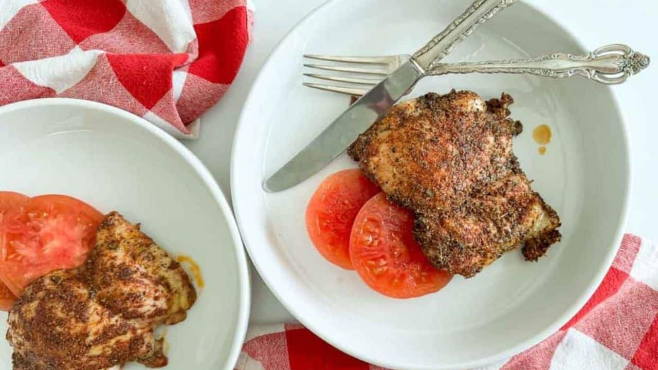 Chicken coated in seasoning on a plate with tomatoes.