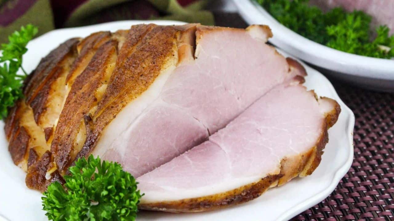 Sliced baked ham on a white plate, garnished with fresh parsley.