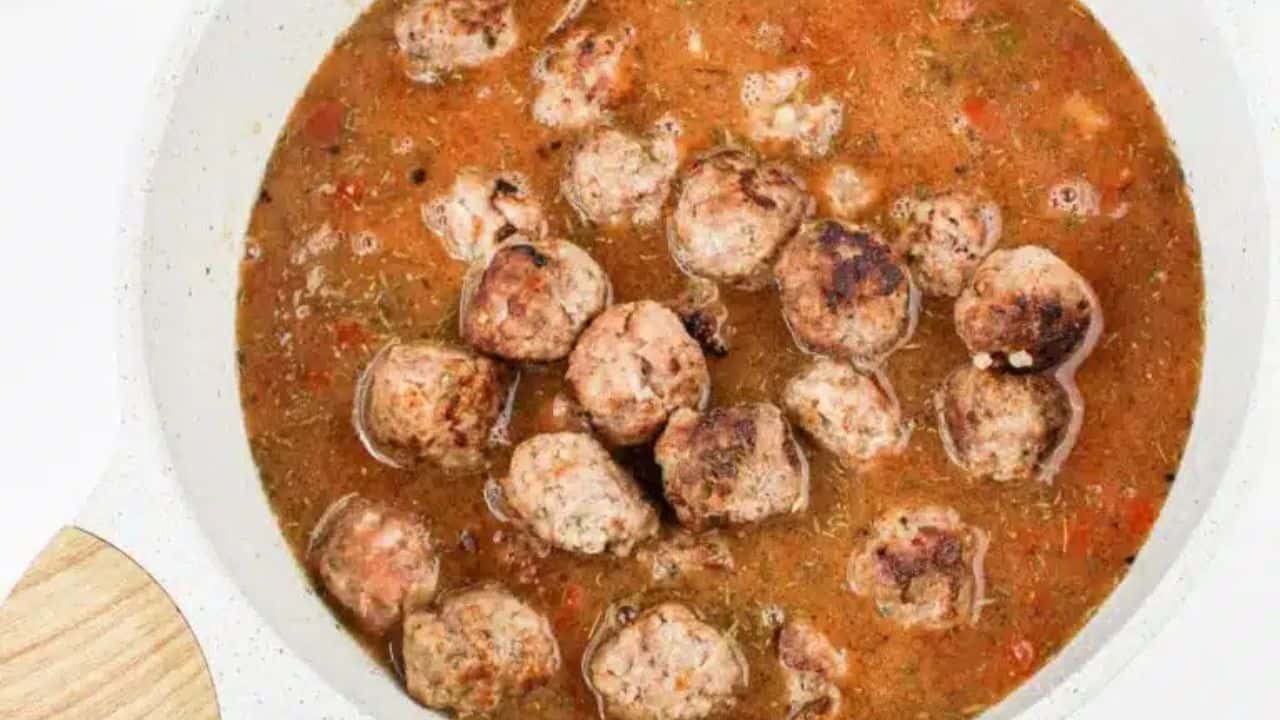 A bowl of rice and meatball stew with vegetables, served with a spoon, placed on a green checkered cloth.