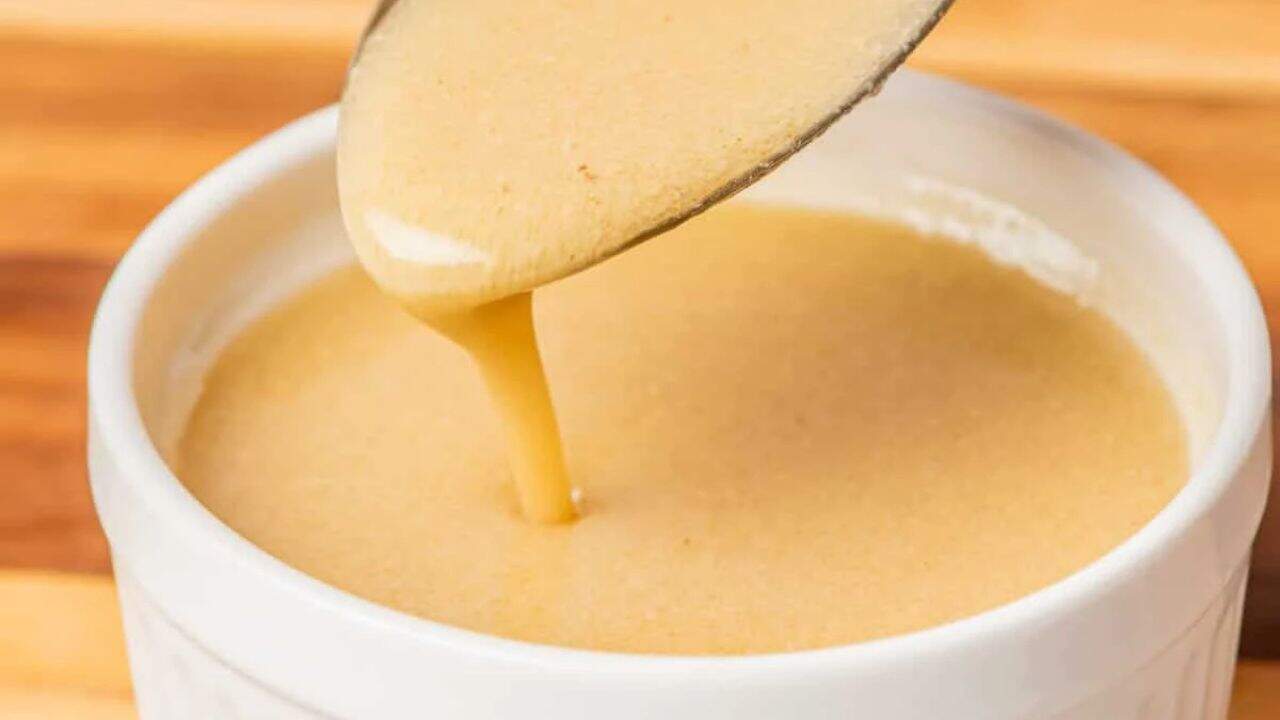 A clear glass gravy boat filled with Champagne vinaigrette on a white surface.