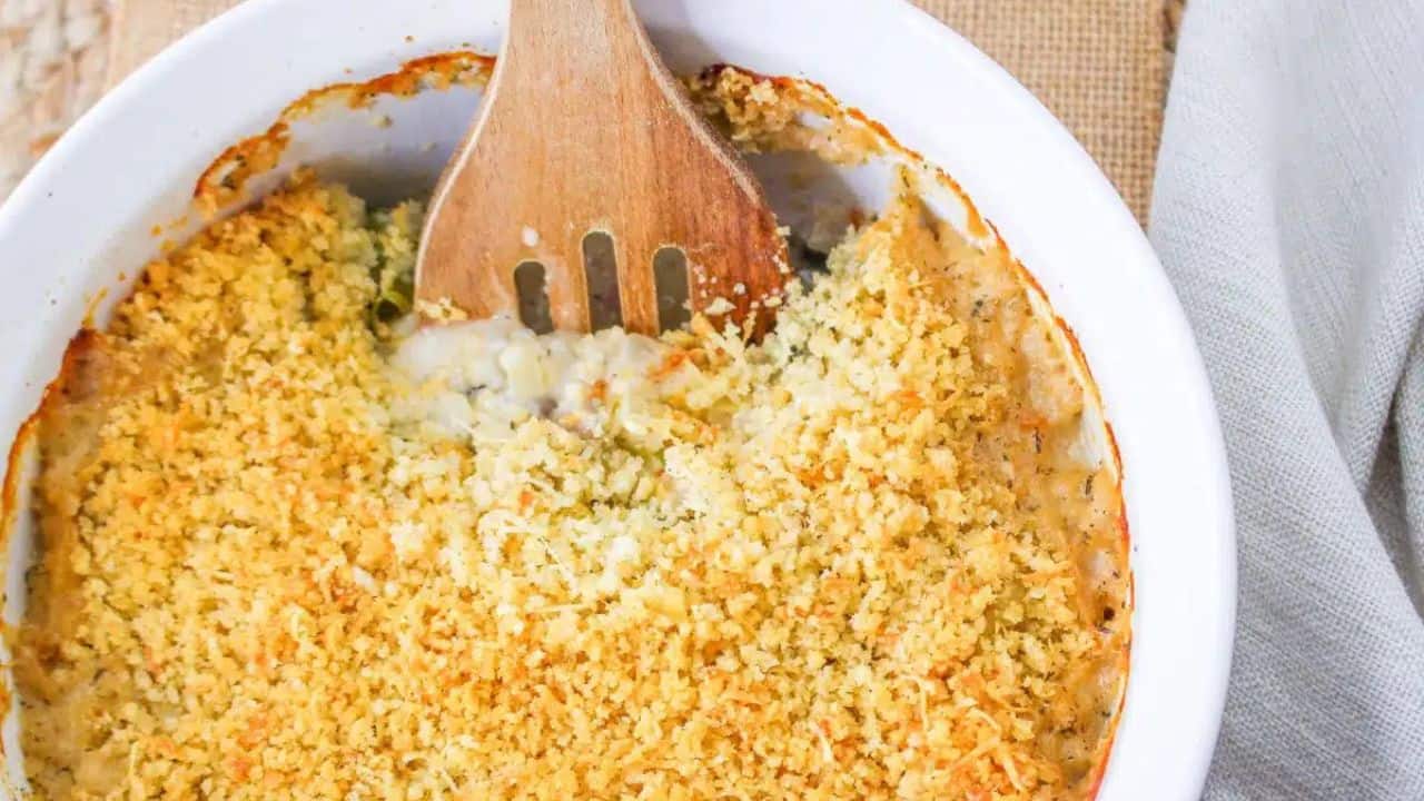 A plate of Brussels sprouts casserole topped with breadcrumbs, garnished with red bell pepper pieces, and served with a fork on a cloth background.