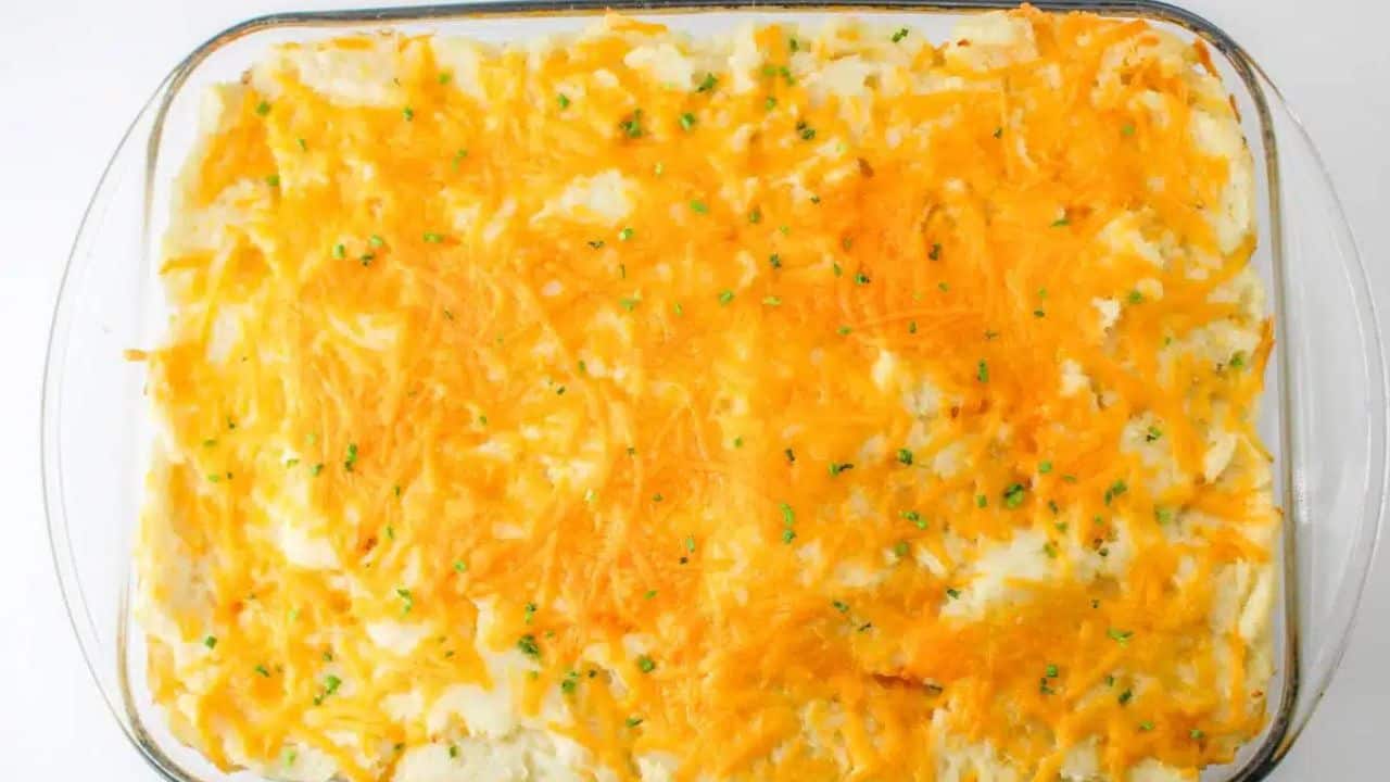 Mashed potatoes and melted cheese, being lifted from a glass baking dish with a spatula.