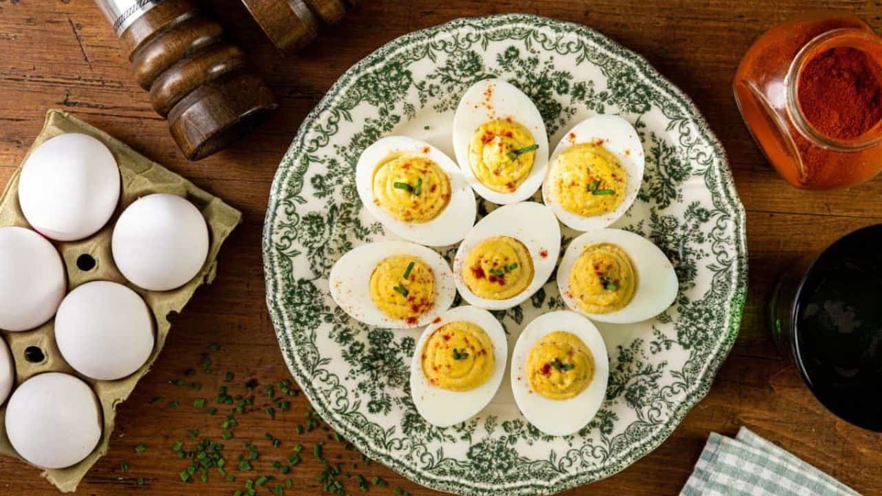 Close-up of Southern deviled eggs on a plate, filled with a creamy yellow yolk mixture and sweet pickle relish, garnished with green chives and a sprinkle of paprika. The eggs are neatly arranged and appear ready to serve.