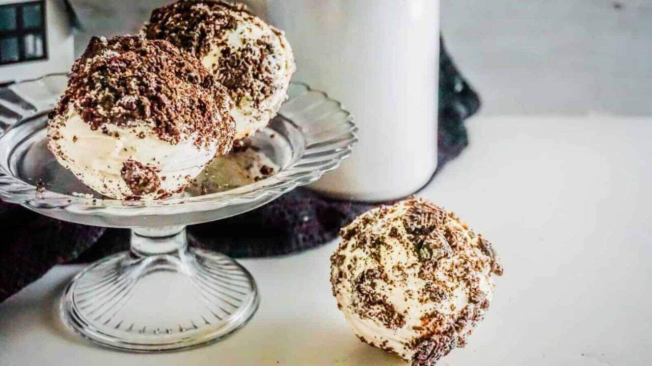 Three indulgent desserts, covered in chocolate crumbles, are displayed with two scoops on a glass dish and one on the table.