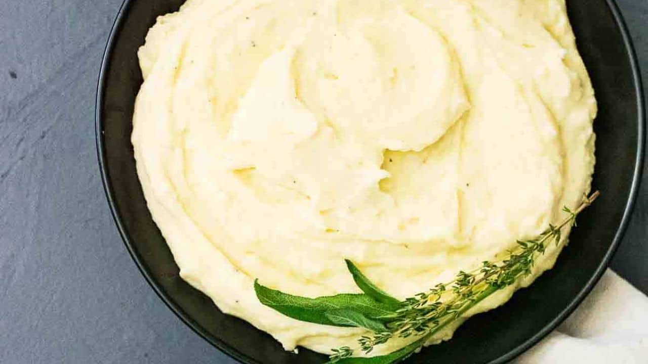 A bowl of mashed potatoes with gravy and sprigs of thyme and sage.