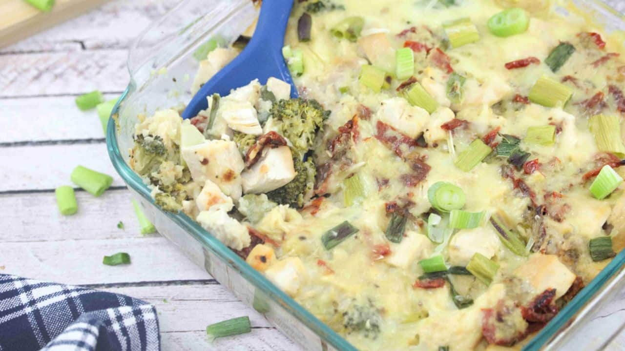 A glass baking dish filled with a chicken and vegetable casserole topped with chopped green onions; a blue serving spoon is in the dish.