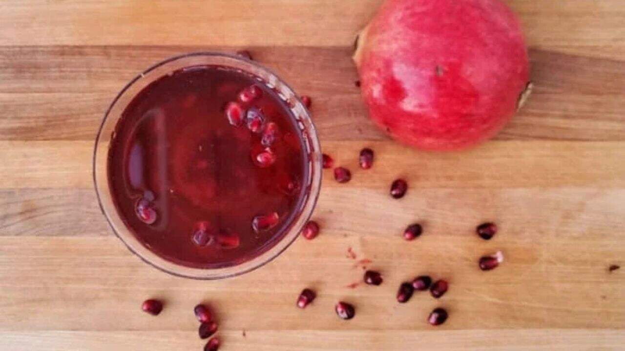 Image shows a martini glass with a Pomegranate Fizz Cocktail and pomegranate arils around it.