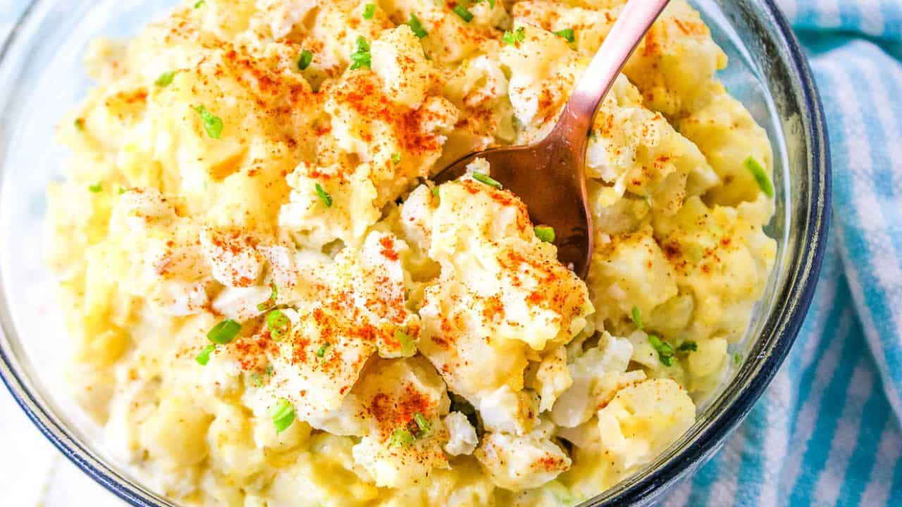 A bowl of creamy potato salad with egg garnished with paprika and chopped herbs.