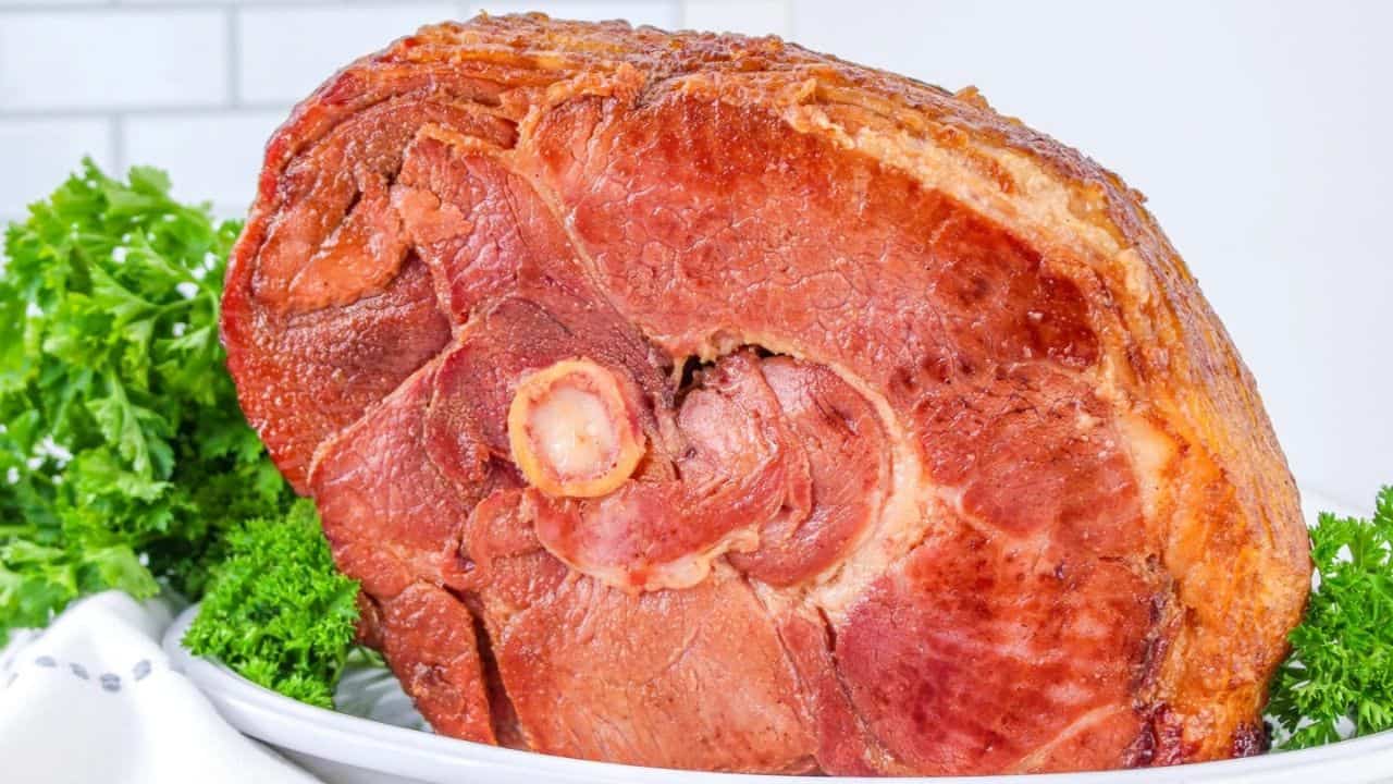 A cooked, glazed ham on a white plate, garnished with parsley.