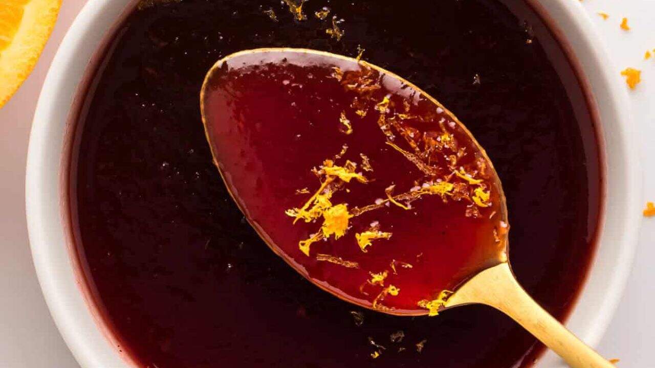 A close up view of cranberry sauce in white bowl, with a spoon and oranges in the background.