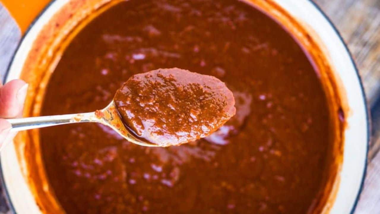 Overhead shot of a pot of enchilada sauce witih a spoonful of enchilada sauce above it.