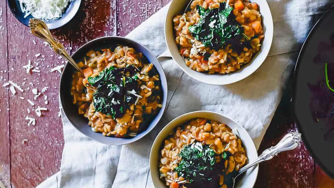 Three bowls of risotto topped with sautéed greens and grated cheese sit on a cloth napkin, with a small dish of shredded cheese nearby on a wooden table.