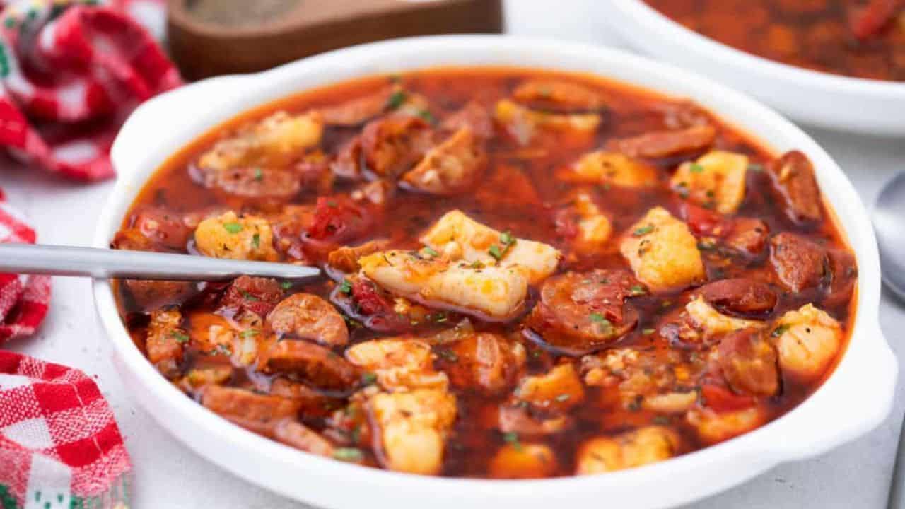 A bowl of soup with sausage and fish.