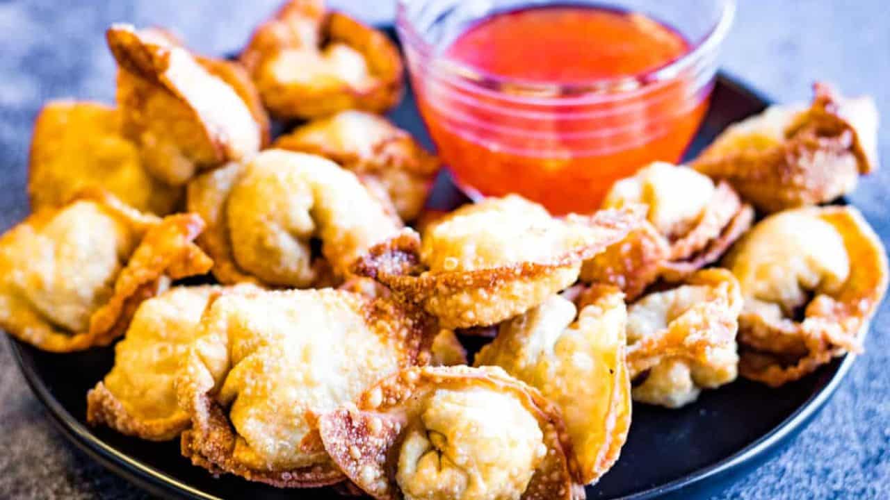Fried wontons on a black plate with dipping sauce.