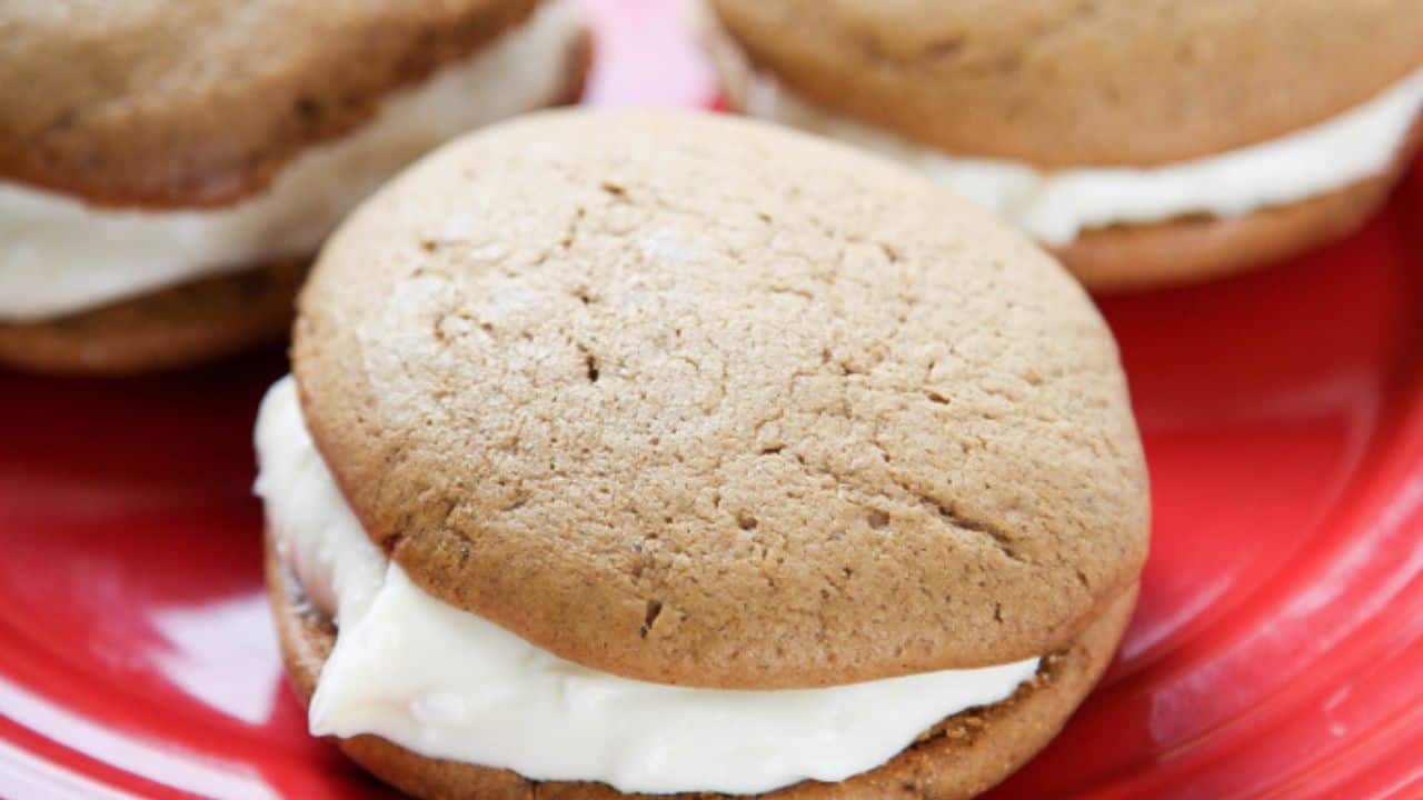 Three whoopie pies with light brown cake and white cream filling on a red plate.
