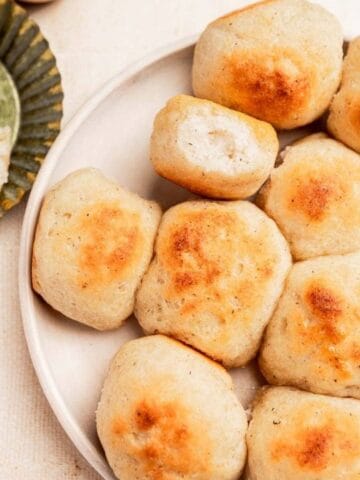 A plate of round, golden-brown biscuits with one biscuit cut open and buttered on a small dish nearby.