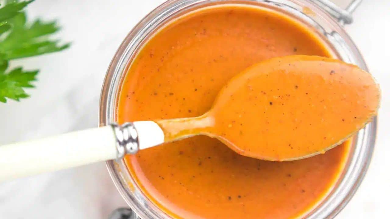Enchilada Sauce in a glass container with a spoon on top filled with sauce.
