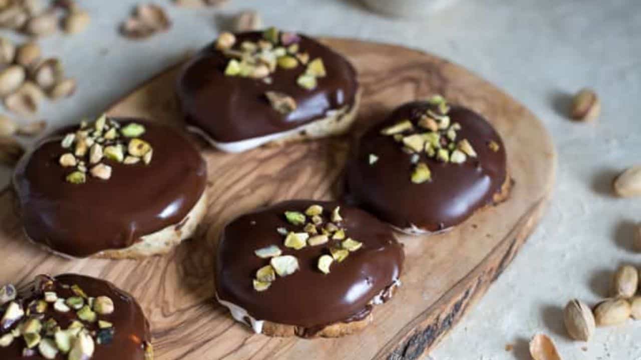 Chocolate covered pistachio cookies on a wooden cutting board.