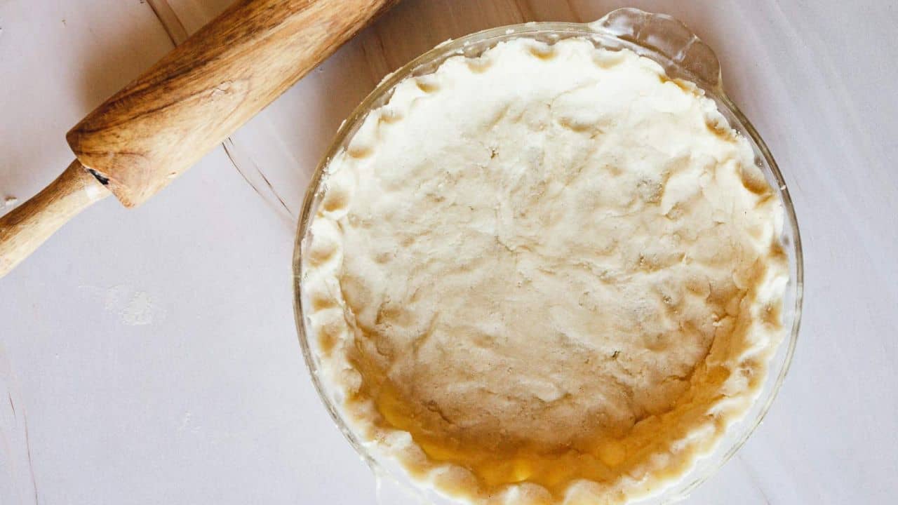 A person rolling out a pie crust in a glass pan.