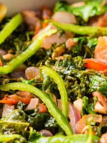A bowl filled with sautéed kale, sliced green bell peppers, chopped tomatoes, onions, and mushrooms.