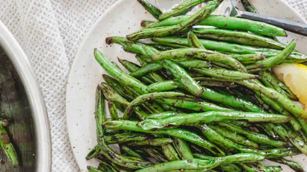 Grilled Asian green beans on a plate with a lemon wedge.