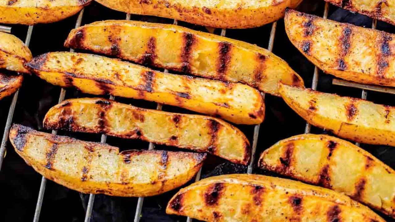 Grilled potato wedges on grates of charcoal grill.
