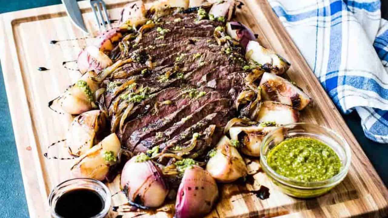 Grilled steak with peaches and onions on a wooden cutting board.