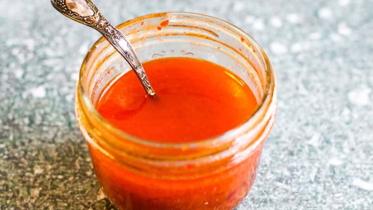 A small clear glass jar filled with a red sauce.