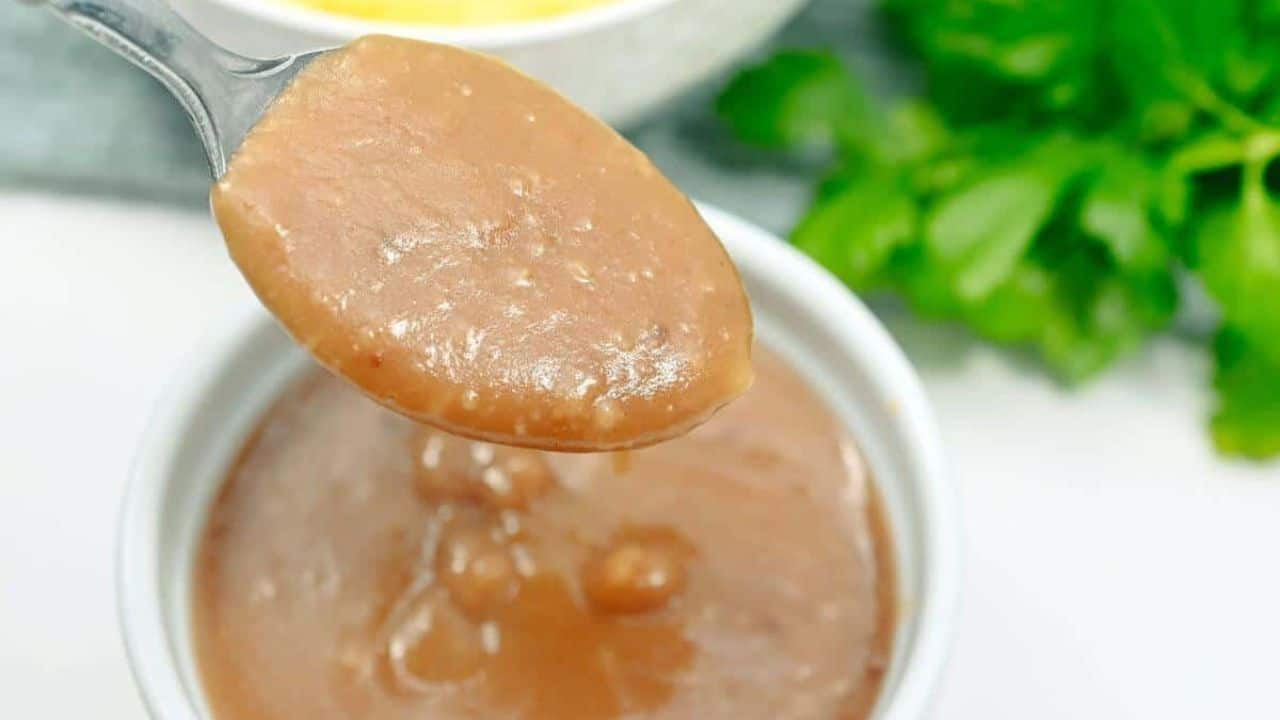 A spoon full of gravy in a white bowl.