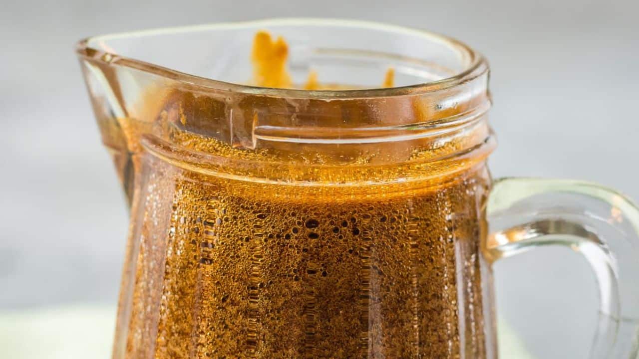 A clear glass pitcher filled with a bubbly, dark brown liquid, likely a freshly made sauce or marinade, against a neutral background.