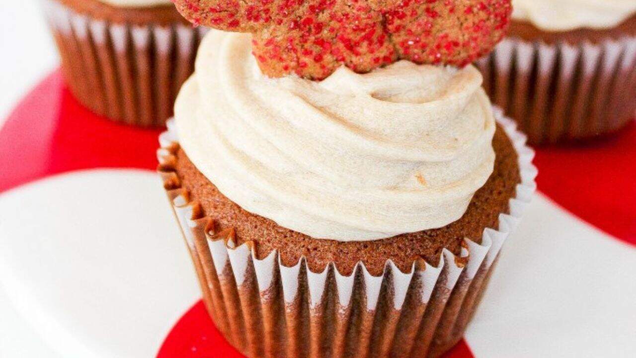 A cupcake with light brown frosting, topped with a cookie shaped like a leaf and sprinkled with red sugar, on a red and white plate.
