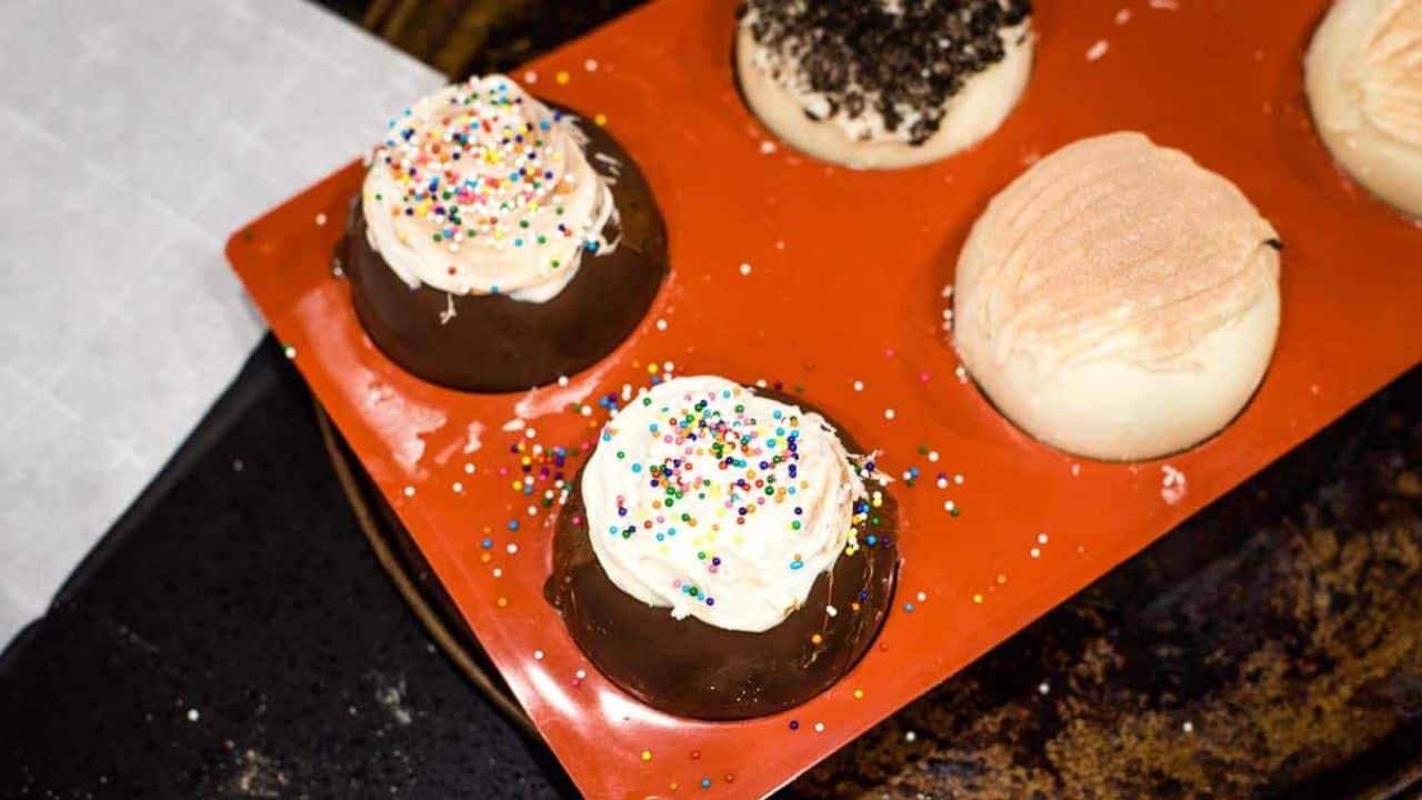 An overhead view of a table spread with hot cocoa, hot chocolate bombs, cookies, and marshmallows on a light blue background.