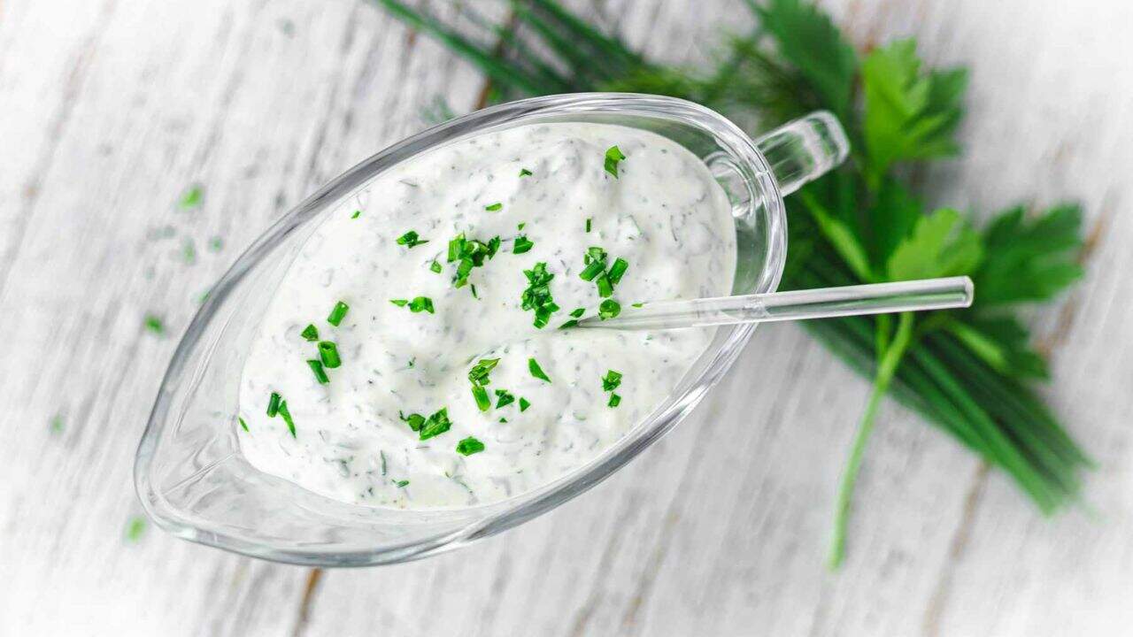 Ranch dressing in a glass bowl with a stick of veggie.