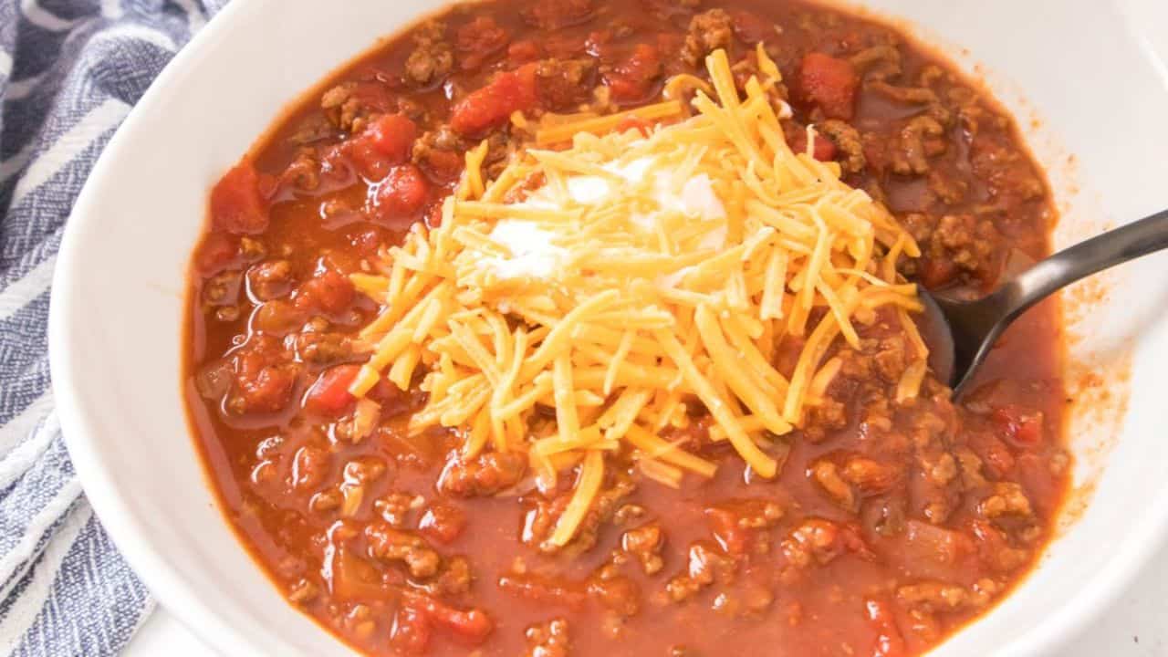 A bowl of chili with shredded cheese in a white bowl.