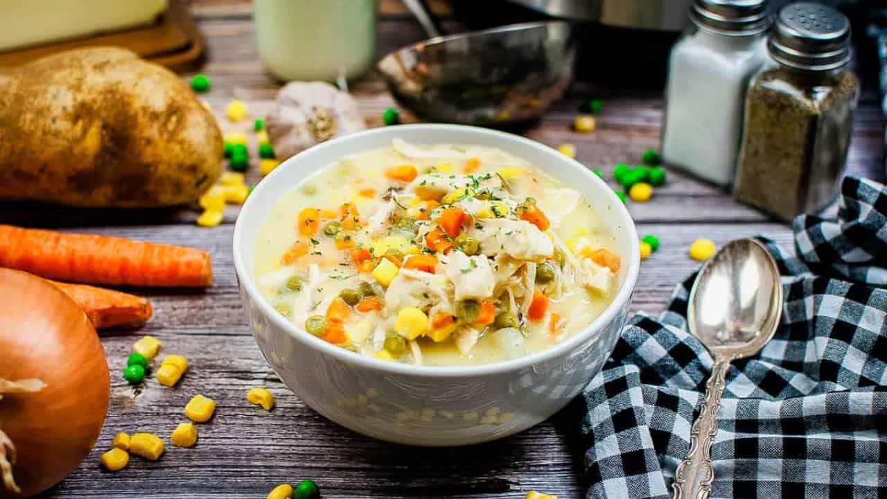 Low angle shot of a bowl of chicken pot pie soup with ingredients scattered around and an instant pot in the background.
